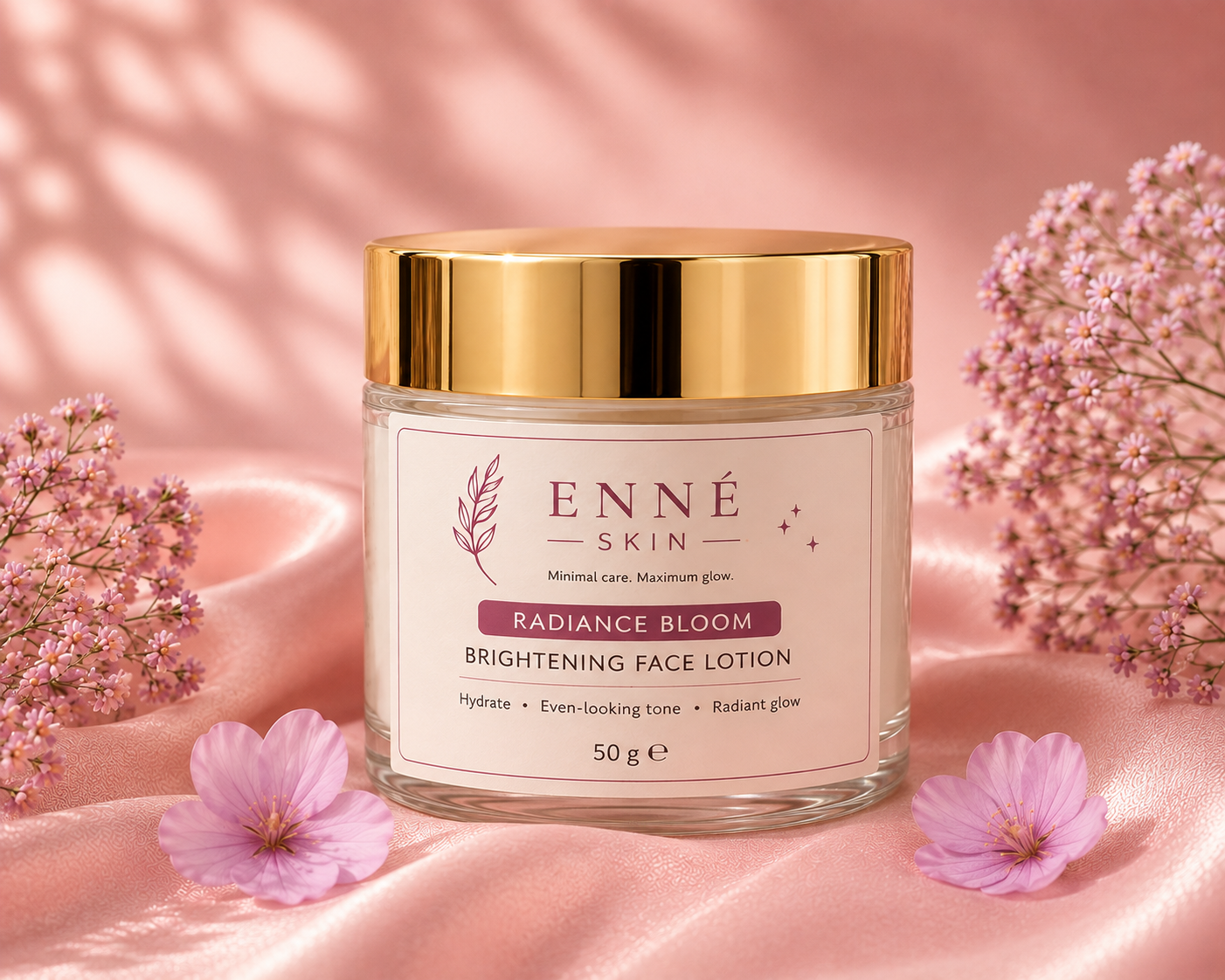 A jar of ENNÉ SKIN Radiance Bloom Brightening Face Lotion with a shiny gold lid and cream-colored label, set on pink satin fabric with pink flowers.